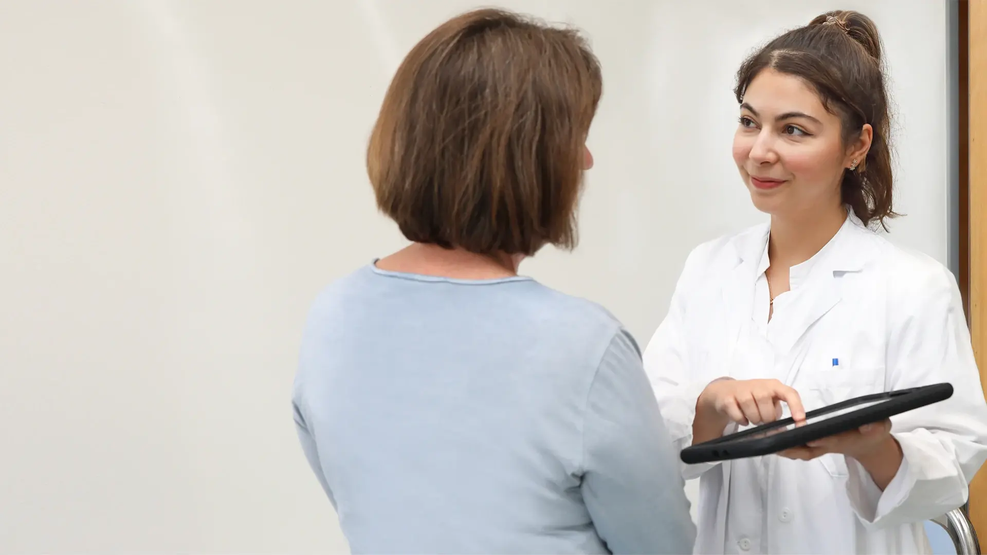Eine Mitarbeitende zeigt einer Patientin Befunde am Tablet.